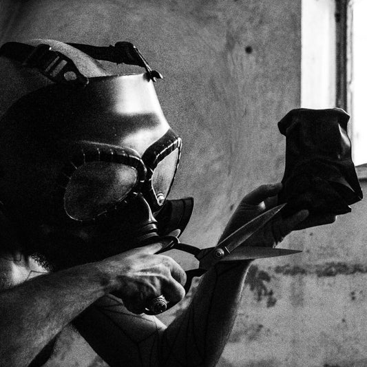 Person wearing a welding helmet and gloves holding a pair of scissors in a workshop.